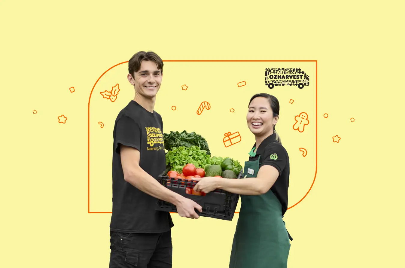 A man wearing an ozHarvest tshirt and woman wearing a Woolworths uniform, holding a crate filled with fresh vegetables