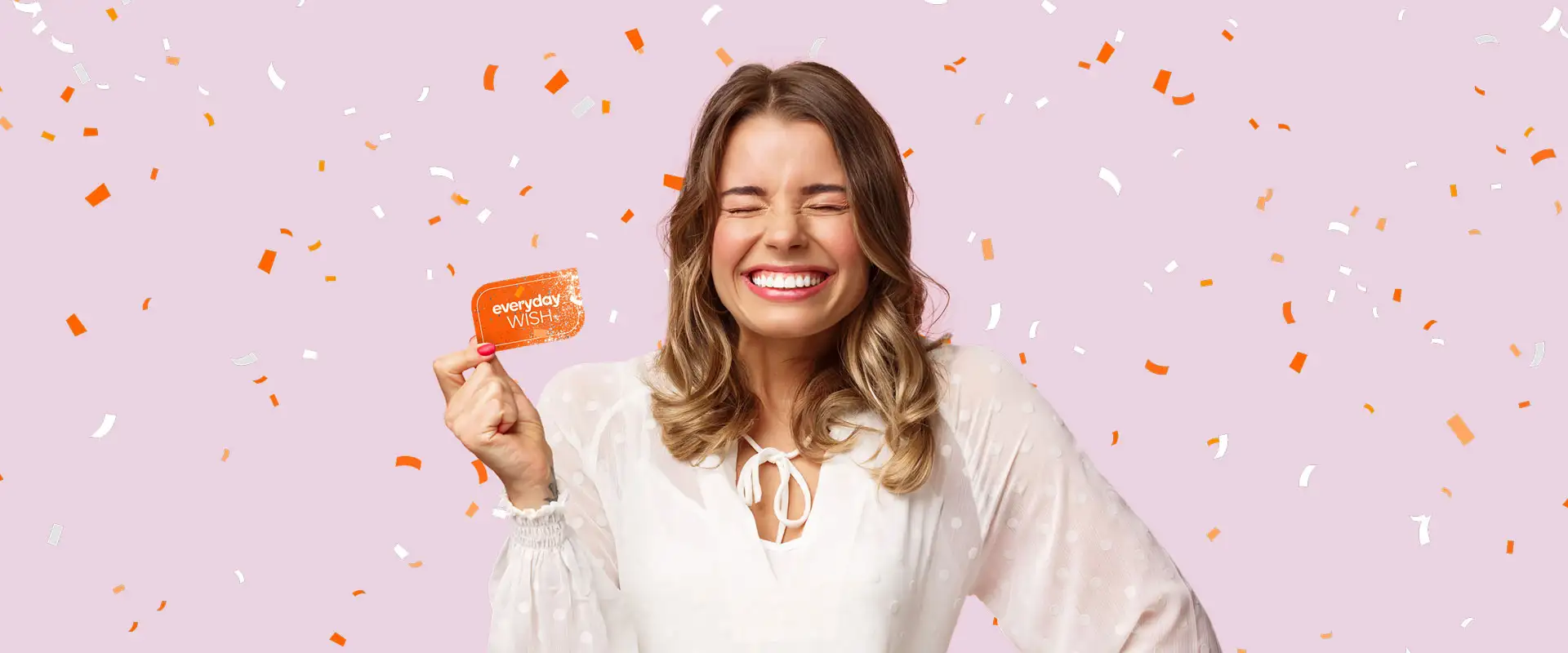 A smiling woman holding an everyday WISH Gift Card on a pink background with confetti.